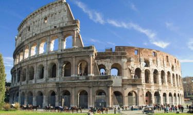 The Colosseum in Rome, Italy is one of the most famous historical buildings and architectural wonders.,a photo of the ancient building stands tall against blue sky with green grass at its base. people can be seen walking around or sitting on horse-drawn carriages to visit it.